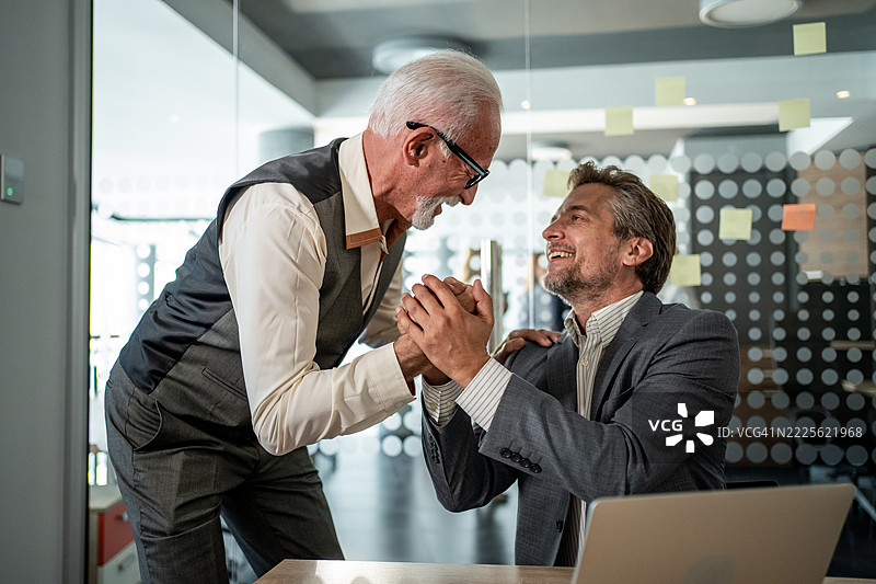 中年和老年商人在现代办公室握手图片素材