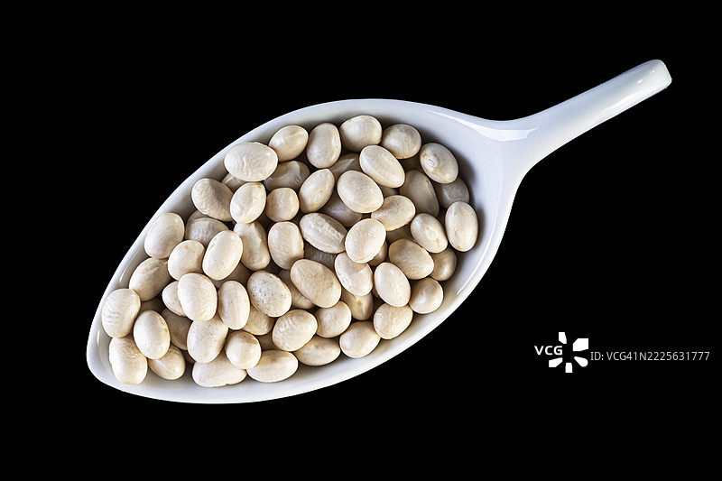 黑色背景上的瓷勺与生干白豆。图片素材
