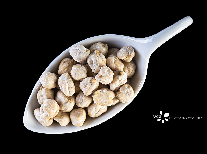 黑色背景上的瓷勺与生干鹰嘴豆。图片素材