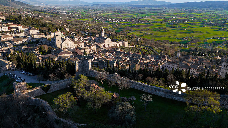 从马焦雷城堡俯瞰意大利翁布里亚地区阿西西历史中心和山谷的日落景色，古老的石墙、教堂和乡村，黄金时刻的遗产旅行照片图片素材