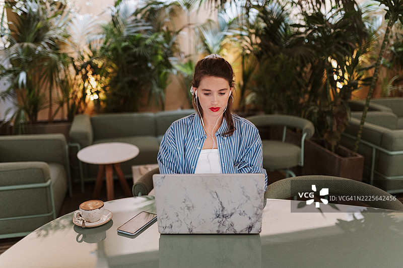 女性博主在咖啡馆舒适的氛围中专注于笔记本电脑工作的正面视图图片素材