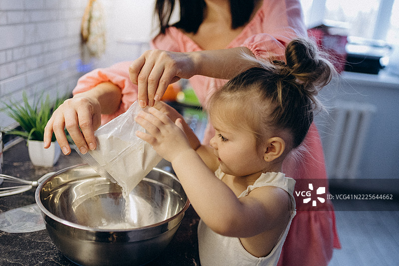 母女在厨房一起倒面粉到碗里，进行烘焙活动图片素材
