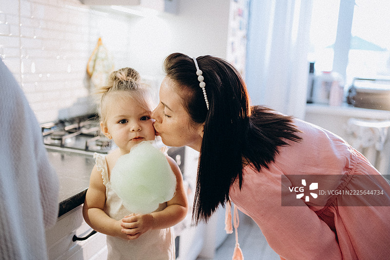 慈爱的母亲在厨房亲吻手里拿着棉花糖的女儿图片素材