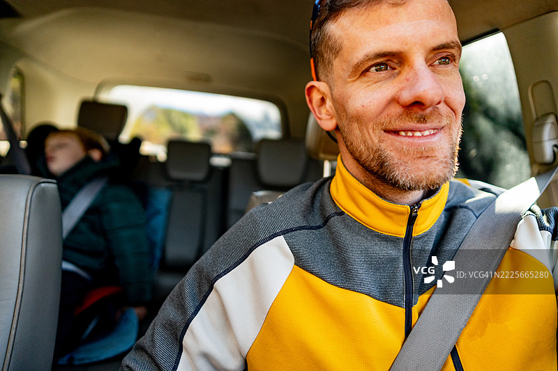 中年男子在公路旅行中驾驶，儿子坐在后座。图片素材