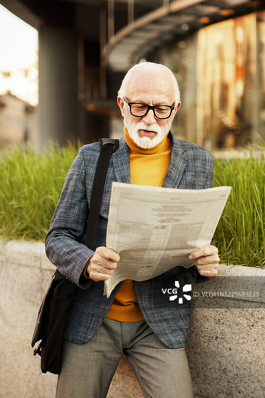一位退休老商人在街上阅读报纸的肖像。图片素材
