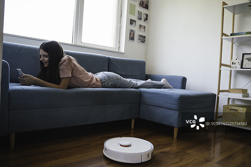 年轻女性使用智能手机与吸尘器图片素材