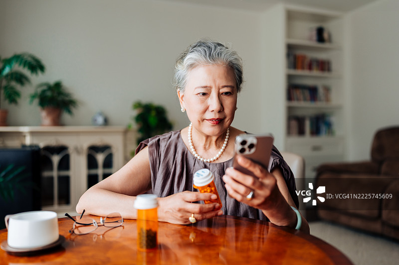 亚洲老年女性在家中通过智能手机与医生进行虚拟预约，咨询她的处方和药物选择。远程医疗、老年人和医疗保健概念。图片素材