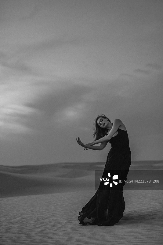 优雅的女性在沙漠中舞蹈，展现出戏剧性的黑白色调图片素材