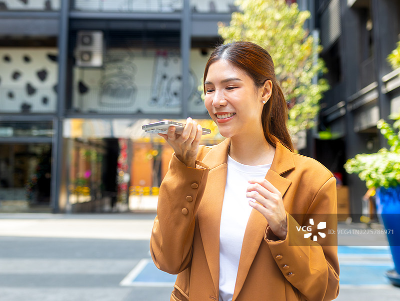 亚洲商务女性使用手机与人工智能语音助手交谈，亚洲女性在智能手机上使用人工智能应用。图片素材