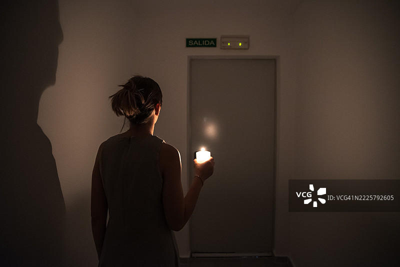 一位面目模糊的女性手持点燃的蜡烛，寻找建筑物的出口，正值停电时刻。图片素材