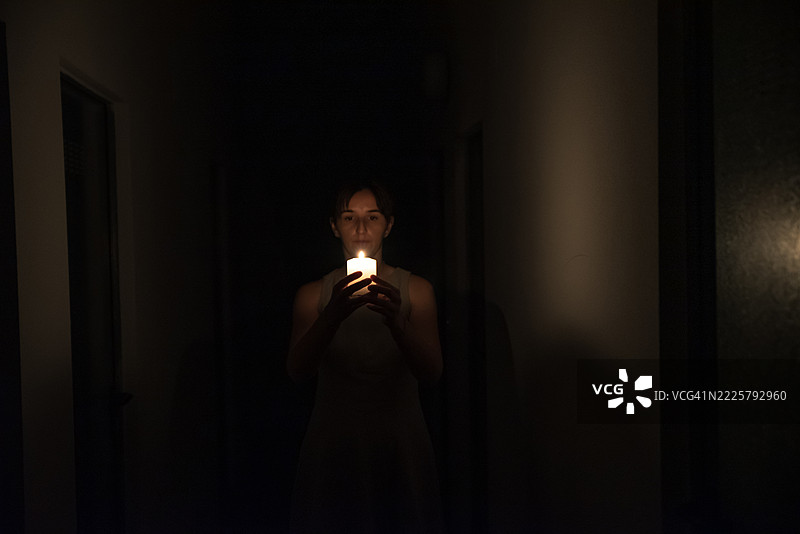 年轻女性在昏暗的走廊中凝视着点燃的蜡烛光。图片素材
