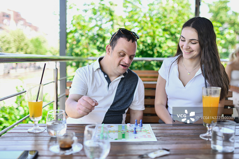 在户外玩飞行棋时，支持的朋友与唐氏综合症男孩一起欢笑图片素材