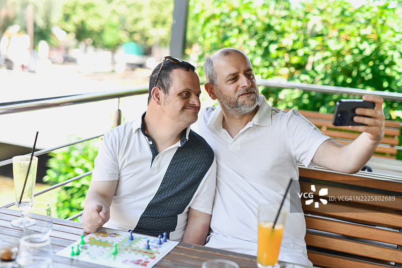 快乐的兄弟们在户外咖啡店里拍自拍，同时玩着飞行棋游戏图片素材