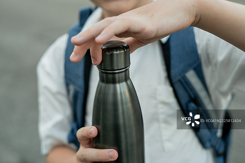 背着书包的男孩正在打开一个铁水瓶。开学季。学习。图片素材