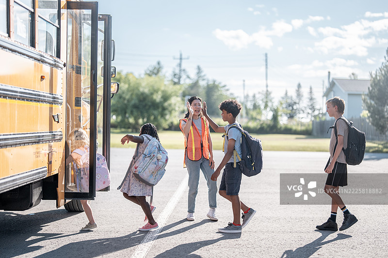 学生在明亮阳光明媚的早晨，在监督下登上校车图片素材