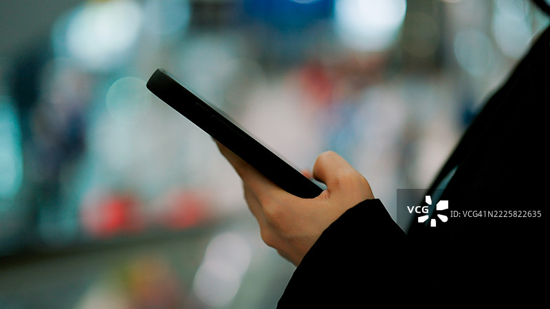 年轻的亚洲女商人在机场的自动人行道上微笑着使用手机。图片素材