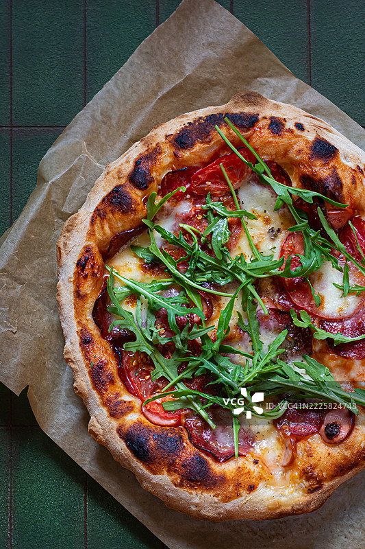 意大利香肠、火腿、番茄酱和香草的比萨饼，背景为绿色。地中海美食。图片素材