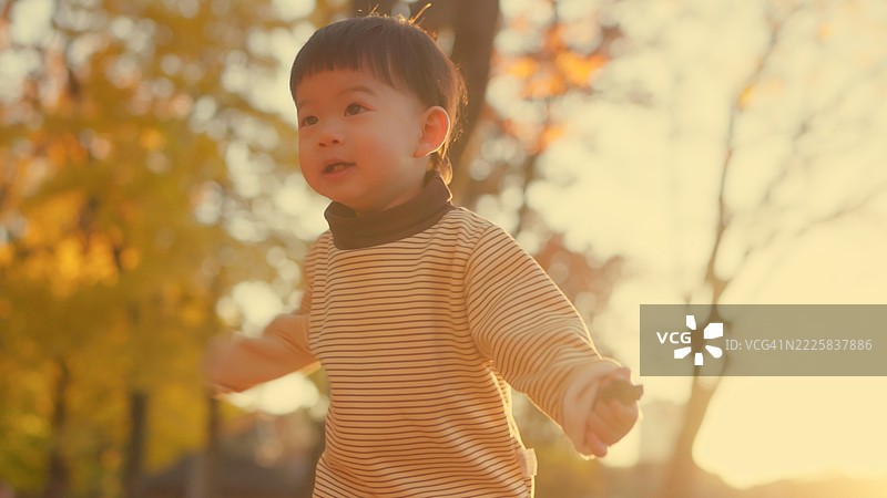 亚洲幼儿男孩在冬季黄昏的公园里学习走路，玩耍奔跑，享受生活。图片素材