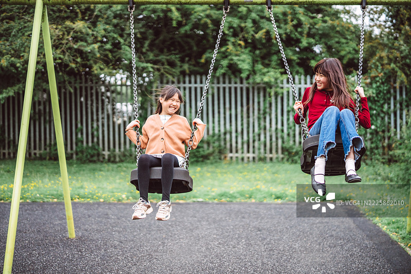 姐妹们在公园的秋千上欢笑在一起图片素材