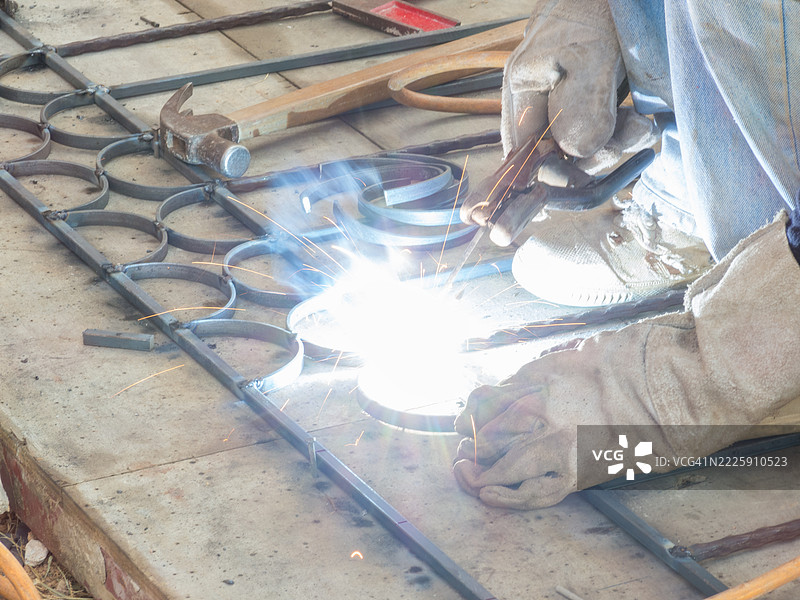 一位铁匠正在弯曲铁壳，以便将它们焊接在一起，形成一个铁栅栏。接下来是美丽的。图片素材