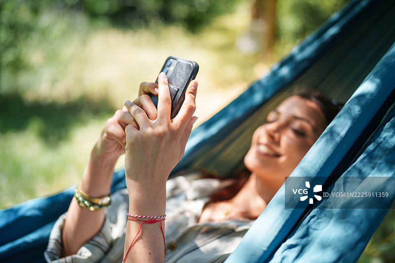 年轻女性在花园的吊床上使用手机图片素材