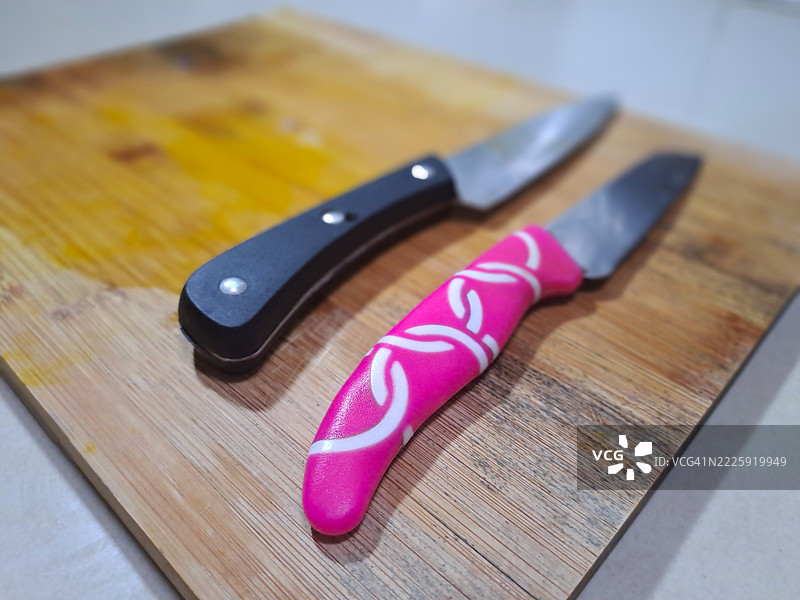 两把刀放在木质切菜板上（黑色和粉色刀具）图片素材