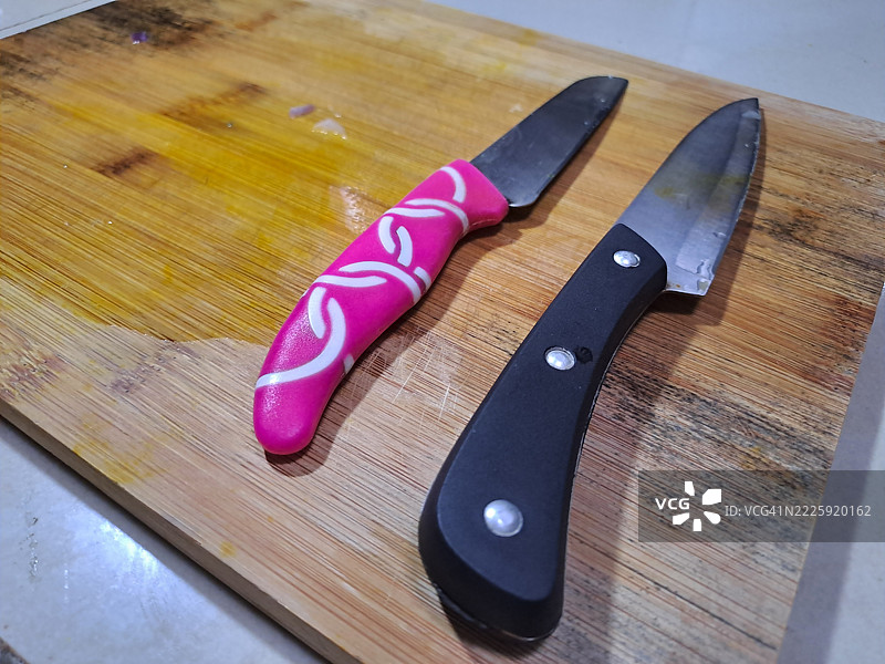 两把刀放在木质切菜板上（黑色和粉色刀具）图片素材