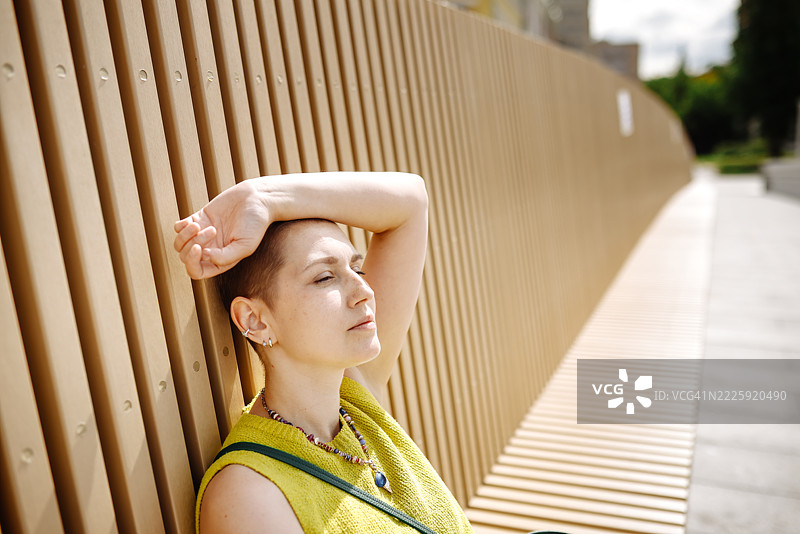 城市中放松和恢复的女性在化疗后坐在长椅上取暖。图片素材