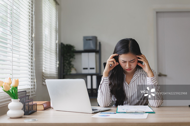 感到压力的亚洲女商人在办公室工作时头痛图片素材