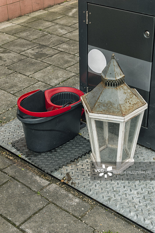 黑色塑料洗衣桶和一个金属灯架放在地下垃圾容器旁边的户外图片素材