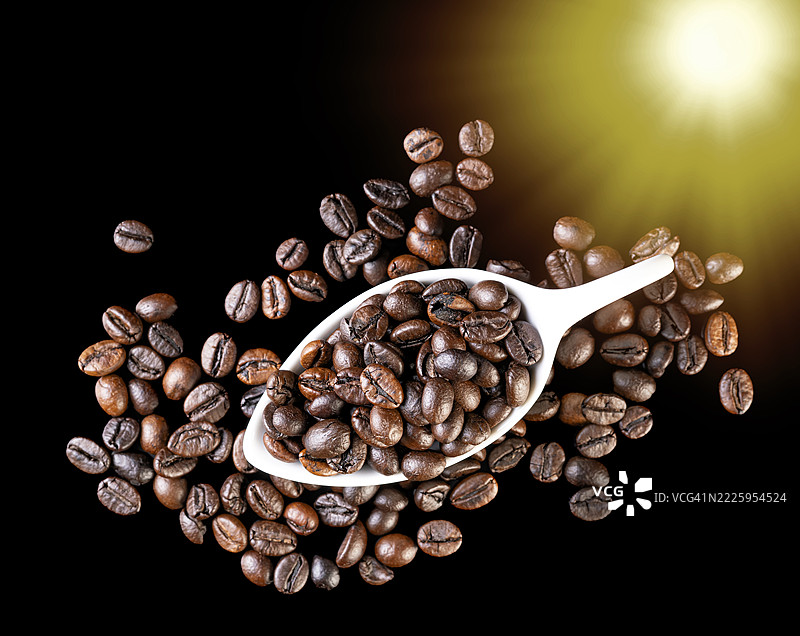 阳光照射下，黑色光滑背景上瓷勺里的烘焙咖啡豆。图片素材