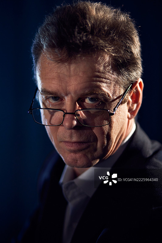 严肃的成熟男性戴着眼镜，背景为黑暗的工作室肖像图片素材