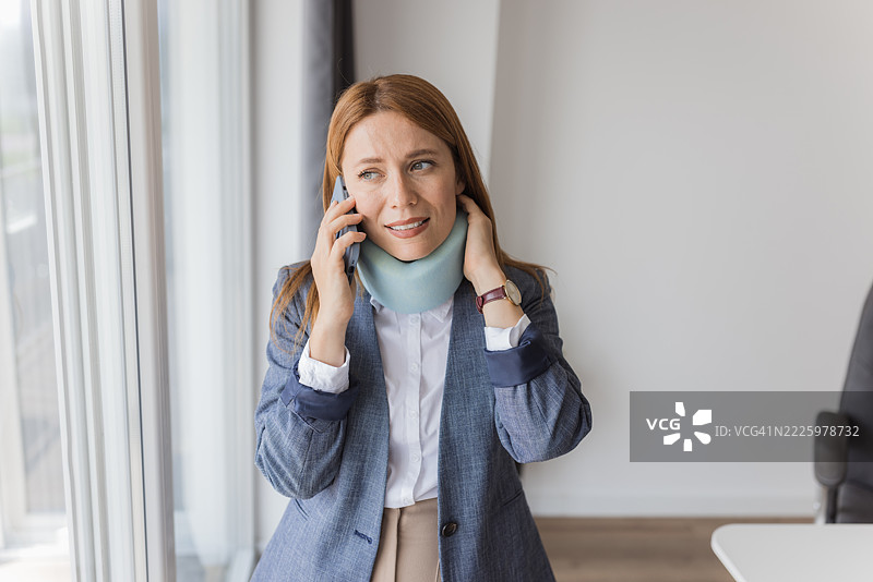 戴着颈托的 व्यावसायिक महिला在办公室里打电话。图片素材