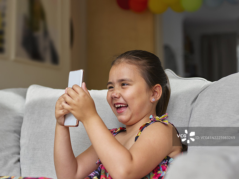 女孩坐在沙发上看智能手机图片素材