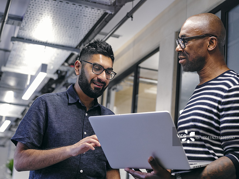 两个男人在办公室走廊里看着笔记本电脑图片素材