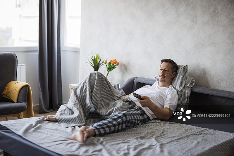 周日早晨，男人在床上放松地看电视图片素材