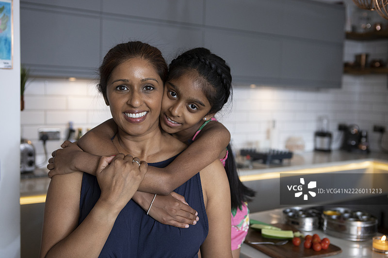 英国，伦敦，女孩在厨房里拥抱母亲的肖像图片素材