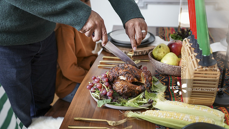 父亲在宽扎节的餐桌上为孩子们（8-9岁，12-13岁）切鸡肉图片素材