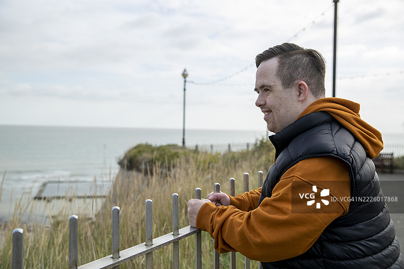 一个男人靠在栅栏上，凝视着海岸。图片素材