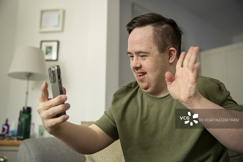 男人坐在沙发上，向智能手机挥手。图片素材