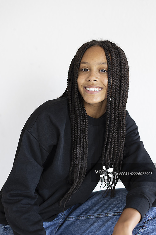 白色背景上微笑的女孩蹲着，手放在膝盖上图片素材