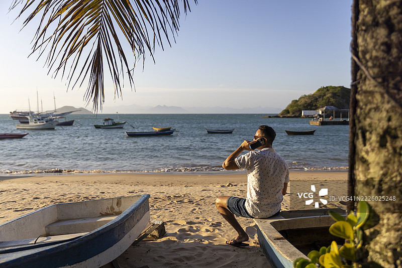 背影的男人坐在海滩上打电话图片素材