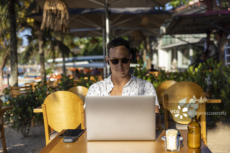 男子在海滩咖啡馆使用笔记本电脑图片素材