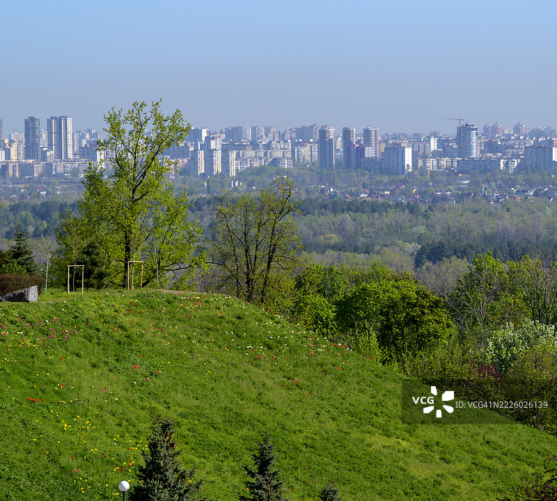 阳光明媚的春天，一座绿丘俯瞰基辅城市天际线图片素材