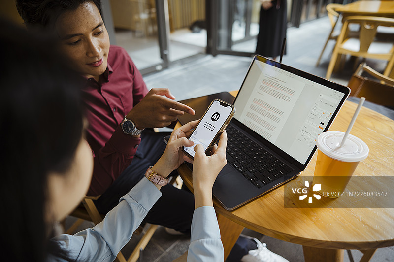 两位不同背景的专业人士在咖啡店使用智能手机和笔记本电脑。图片素材