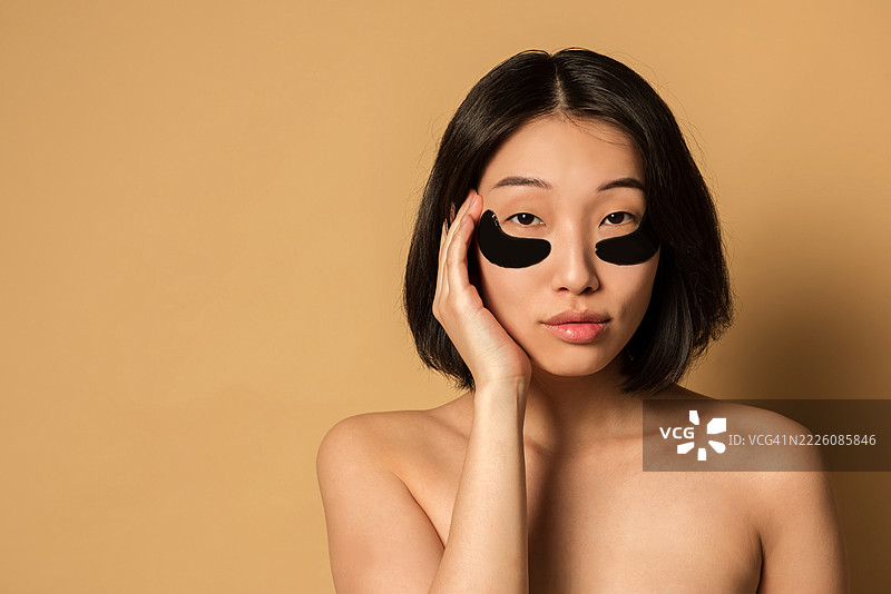 面向镜头的亚洲女性，脸上贴有医疗贴片，清晰的皮肤，摄影棚拍摄。图片素材