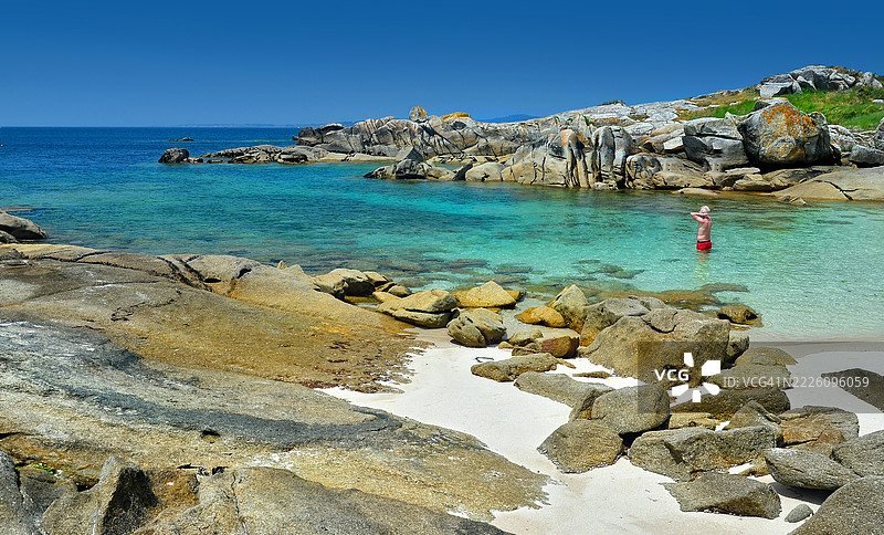 一位单身男子坐在禅宗姿势中，享受着西班牙加利西亚省蓬特维德拉的卡雷龙自然公园内阿鲁萨岛南部美丽海湾的阳光和海滩。图片素材