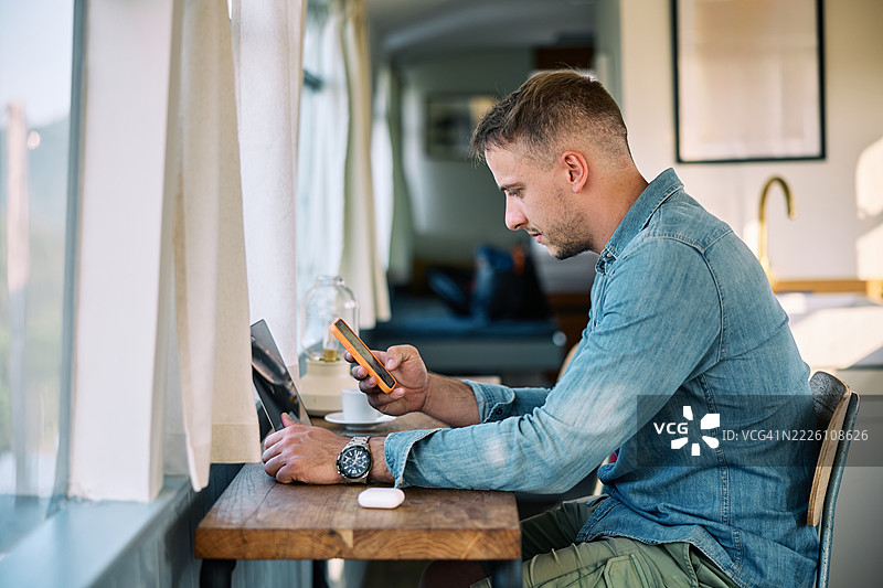 男子在使用笔记本电脑的同时查看手机图片素材