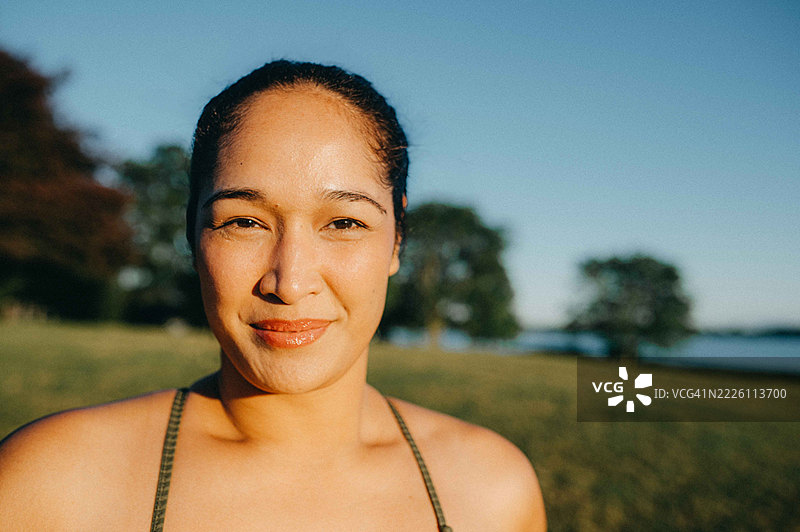 户外一位女性在晴朗的蓝天下微笑着看向镜头，阳光温暖地照耀着她。图片素材