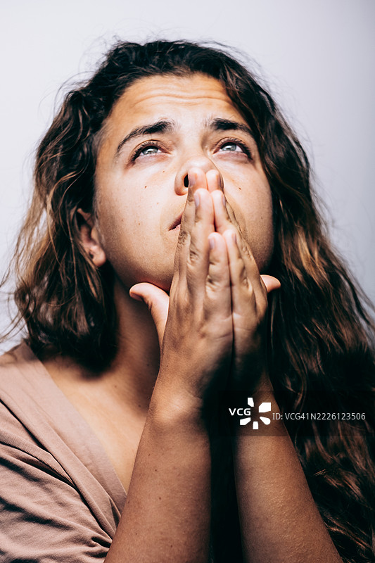 年轻女性双手合十，闭嘴仰望，展现出希望或祈祷的表情。图片素材
